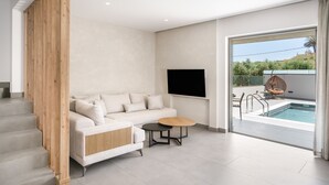 Een moderne woonkamer met een bank, een ronde tafel en een zwembad dat zichtbaar is door een glazen deur.