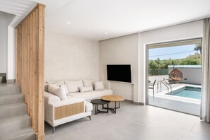 Ein modernes Wohnzimmer mit einer Couch, einem runden Tisch und Blick auf einen Pool durch eine Glastür.