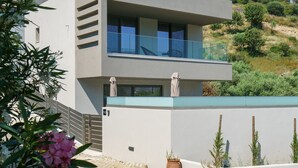Een modern, twee verdiepingen hoog gebouw met een balkon, omgeven door grind en potplanten.