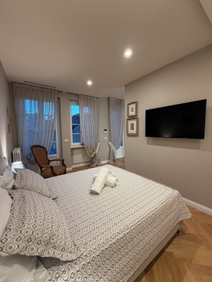 Ein Schlafzimmer mit einem Bett, einem Sessel, einem Fernseher und einem Fenster mit Vorhängen.