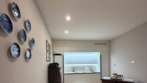 Una sala de estar moderna con un sofá blanco, una mesa de comedor con sillas, una cocina al fondo y platos decorativos en la pared.