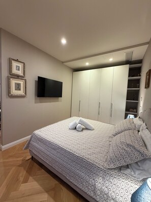 A bedroom with a bed, a TV, a wardrobe, and a shelf with decorative items. - Cozy apartment for 2 people in the heart of Alba. (Alba)