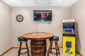 Ett konferensrum med ett runt bord, två barstolar, en darttavla, en tv med Netflix-logotyp och en Pac-Man-spelautomat.
