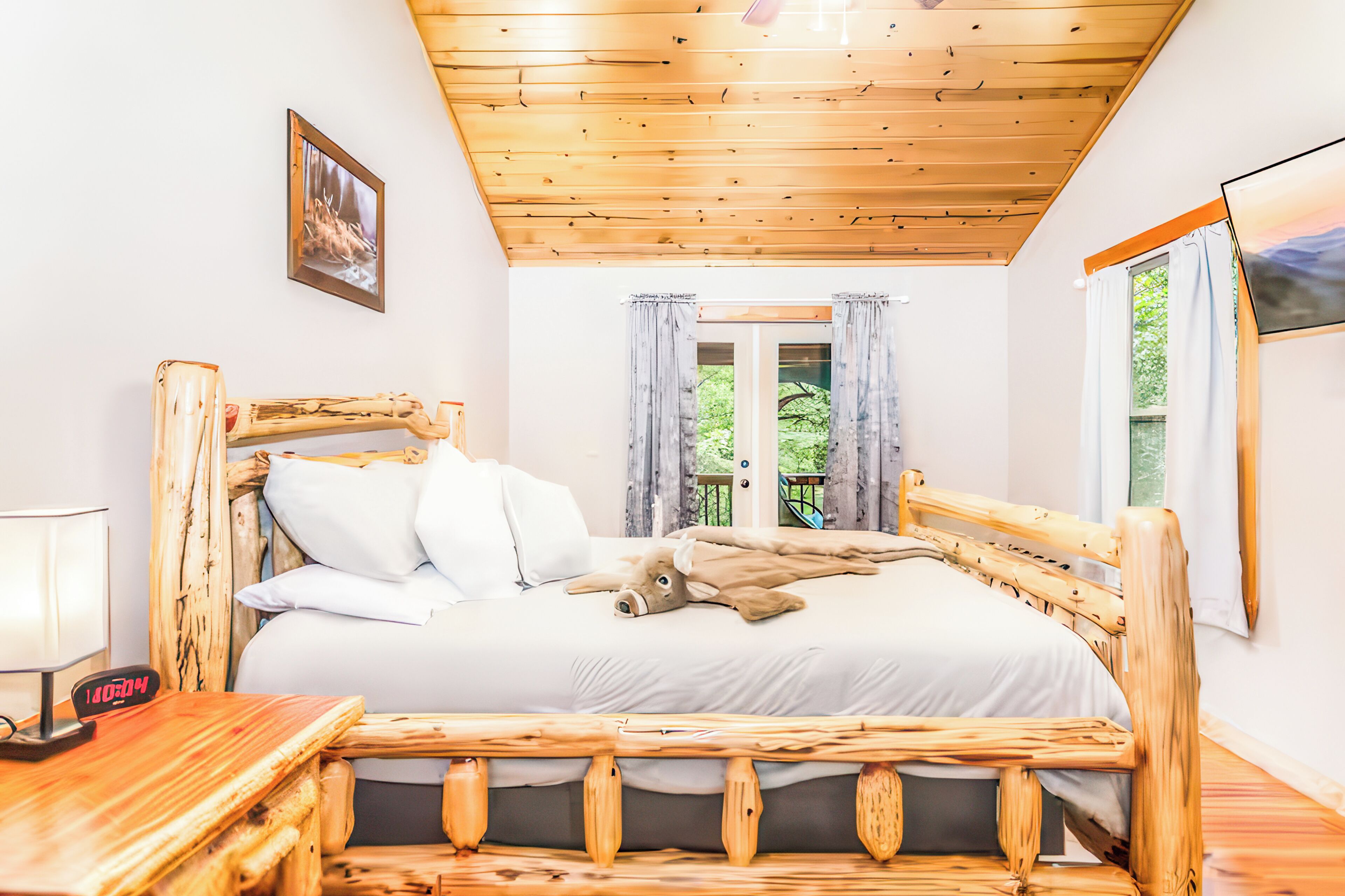 Un lit en bois avec une literie blanche, une table de chevet avec une lampe et une fenêtre avec des rideaux.