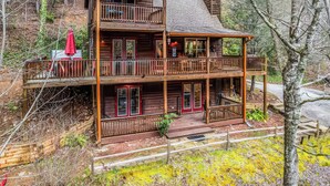 En toetage hytte med balkon, en overdækket veranda og udsigt til den omkringliggende skov.