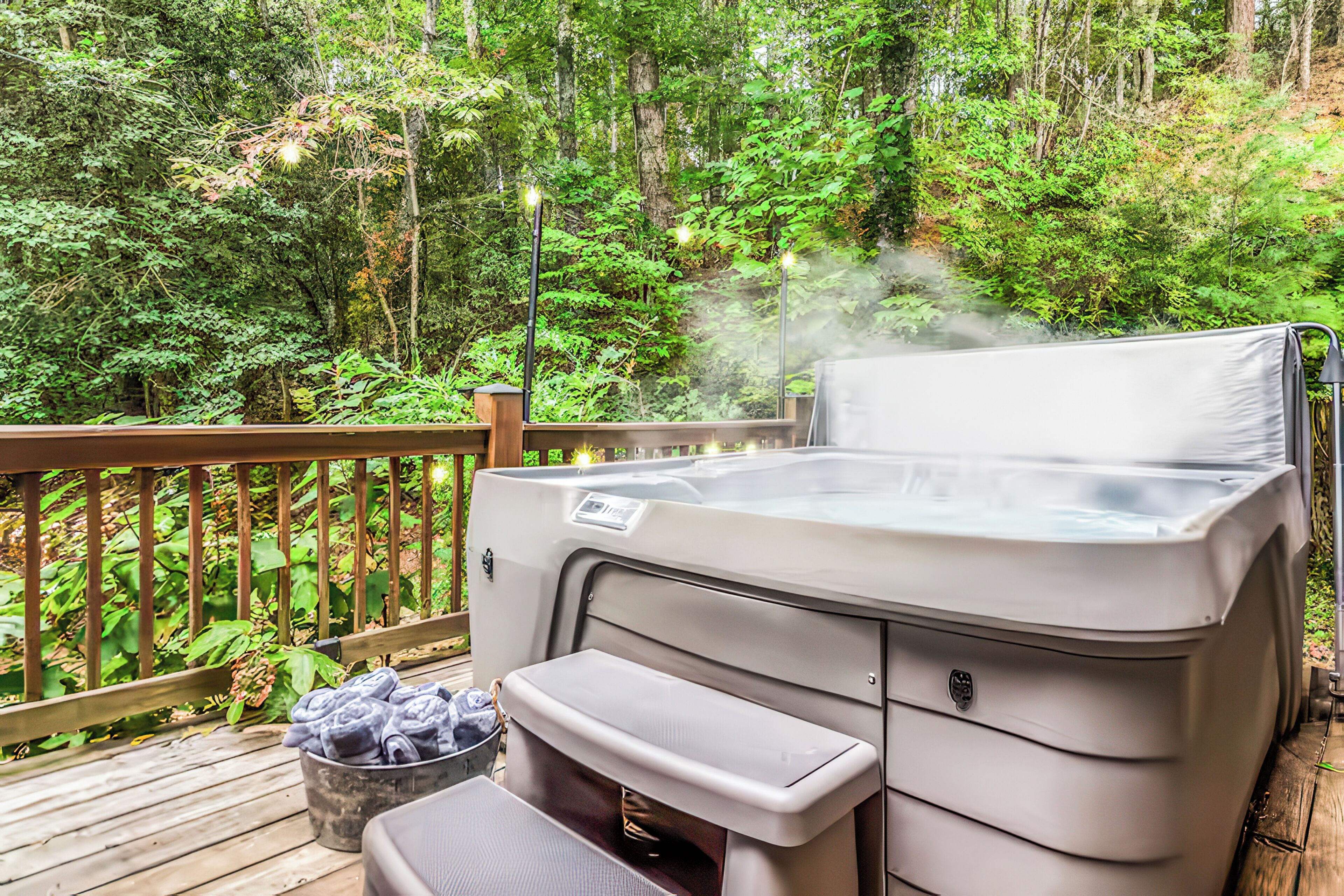 Un bain à remous sur une terrasse en bois, entouré d’une forêt dense.