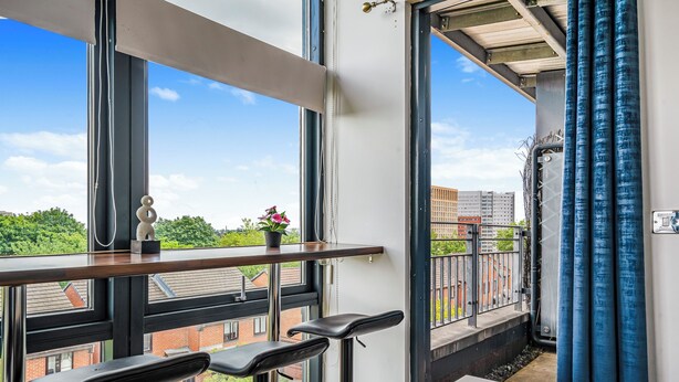 A balcony with a view of buildings and greenery, a table with a bowl and plates, and two bar stools. - Spacious 3BR Duplex | Sleeps 7 | 2 En-Suites | Secure Parking | 3 Balconies (Birmingham)