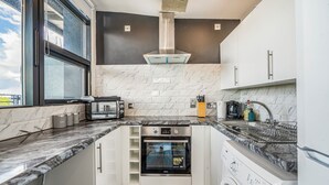 A compact kitchen with a built-in oven, microwave, and washing machine, featuring a marble countertop and modern cabinetry. - Spacious 3BR Duplex | Sleeps 7 | 2 En-Suites | Secure Parking | 3 Balconies (Birmingham)
