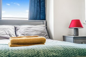 Ein Bett mit einer grün gemusterten Tagesdecke, zwei Kissen und einer gelben Decke.