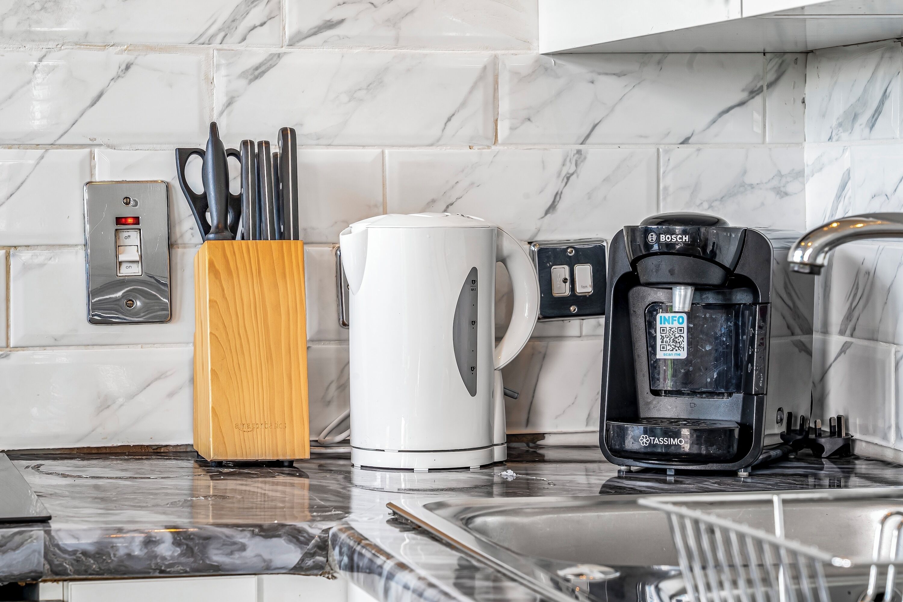 Eine Küche mit Kaffeemaschine, Wasserkocher und Geschirr auf einer Marmorarbeitsplatte.