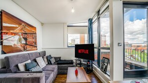 A modern living room with a large TV, a sofa, a coffee table, and a city view. - Spacious 3BR Duplex | Sleeps 7 | 2 En-Suites | Secure Parking | 3 Balconies (Birmingham)