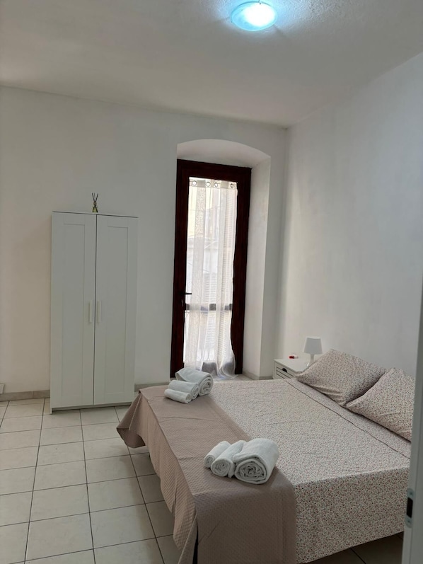 A bedroom with a bed, a wardrobe, a window with curtains, and a bedside table with a lamp.
