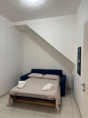 Una cama individual con cabecera, un radiador fijado a la pared y un cuadro enmarcado.