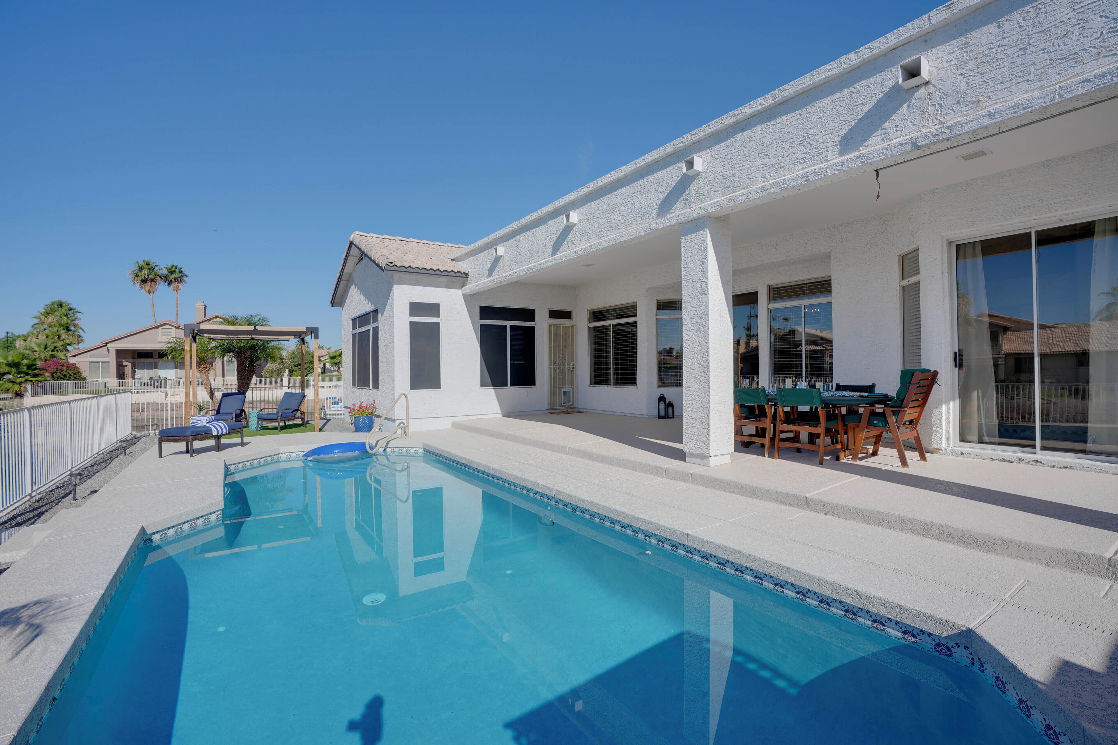 Una piscina con sillas de descanso, un porche cubierto y una zona de comedor con mobiliario de exterior.