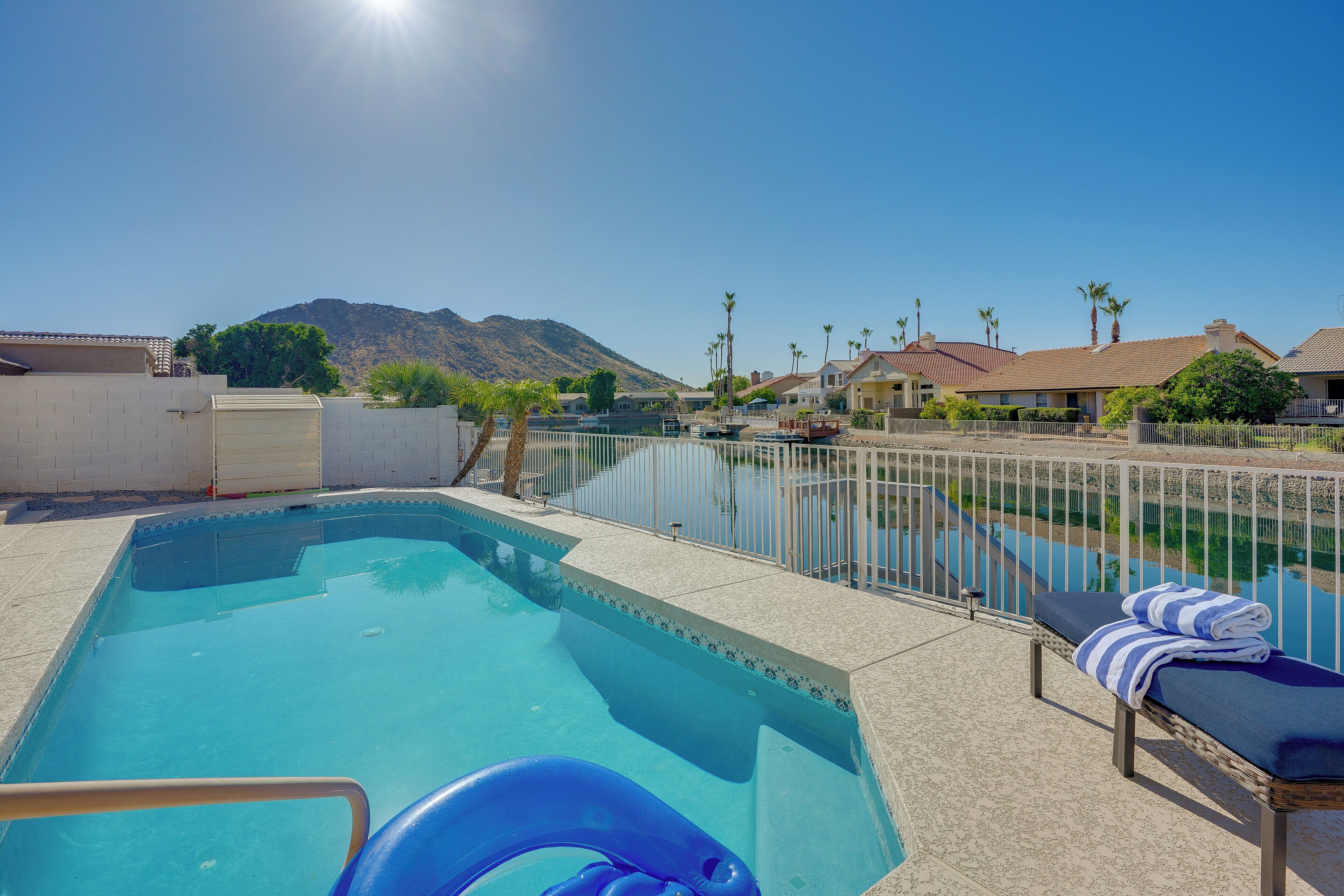 A swimming pool with a lounge area, a view of a mountain, and a clear sky.