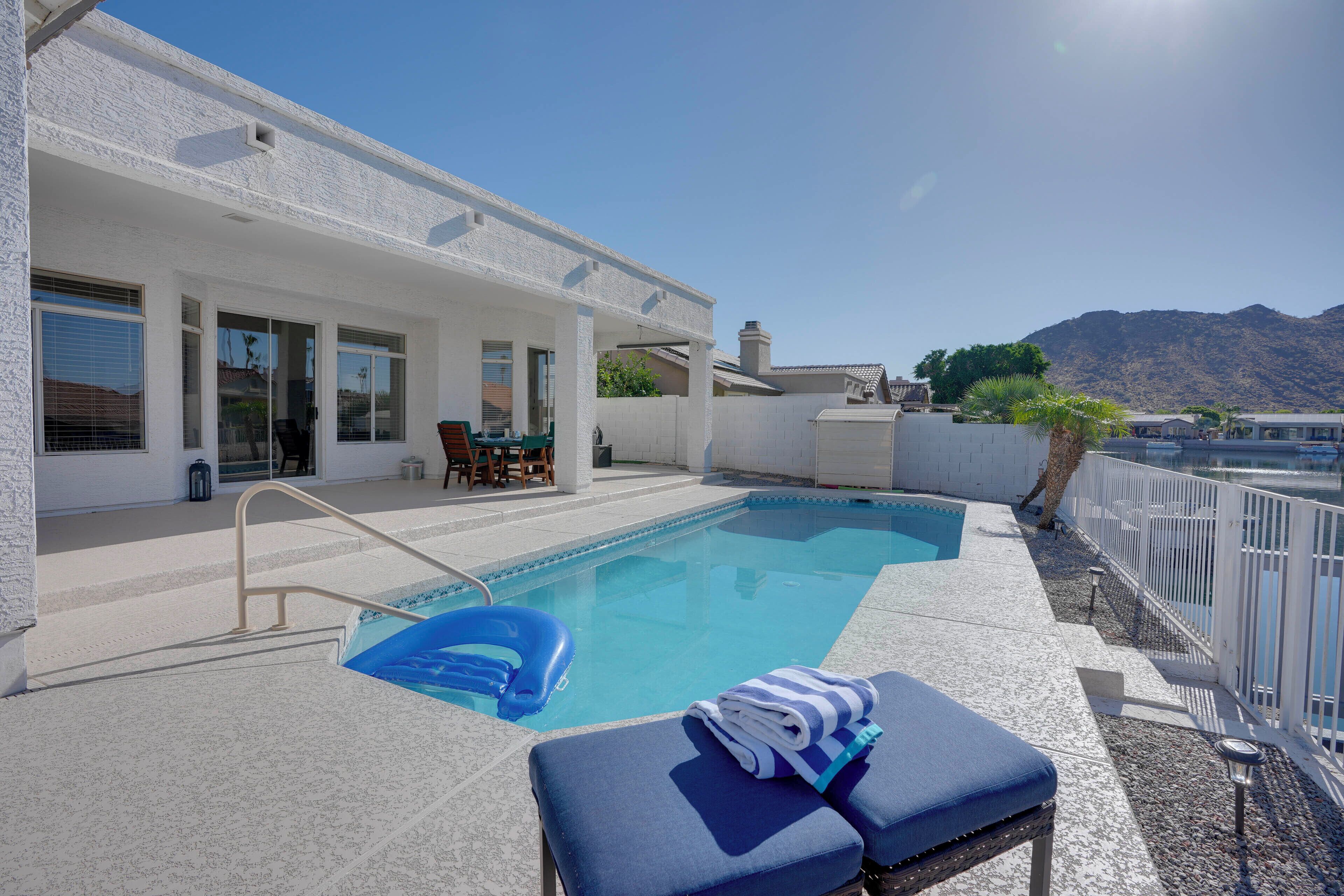 A swimming pool with lounge chairs, a covered patio, and a mountain view.