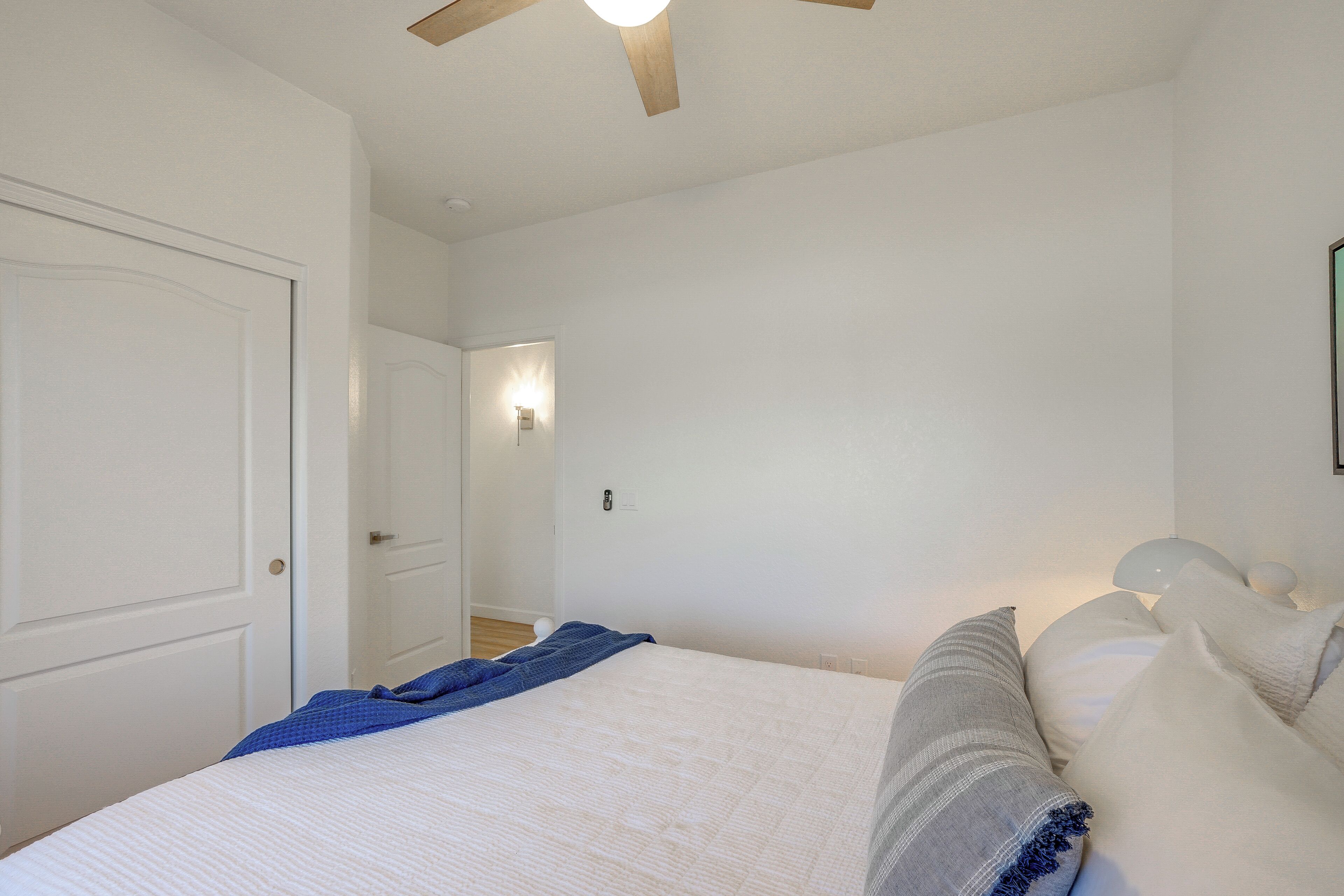 A bedroom with a bed, a ceiling fan, a wall-mounted light, and a door.