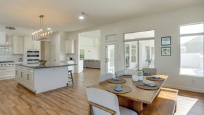 A modern kitchen with white cabinets, a central island, and a dining area with a wooden table and chairs. - Pool + Lakefront: Upscale Glendale Getaway (Glendale)