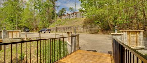 A wooden deck with a metal railing, a paved road, and a stone wall with a wooden fence.
