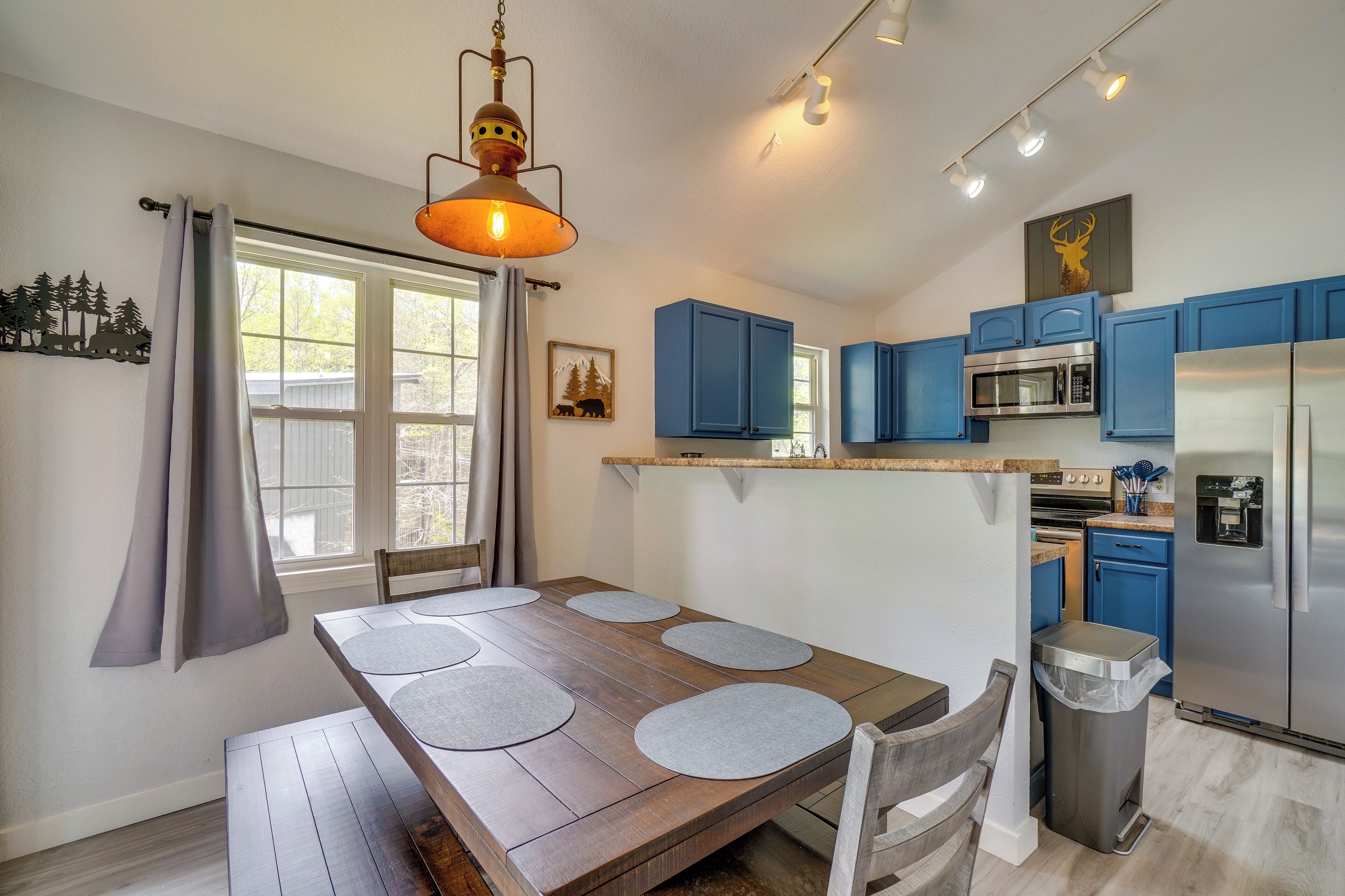 A modern kitchen with blue cabinets, a stainless steel refrigerator, and a dining area with a wooden table and gray placemats.