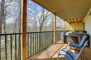 Eine Holzterrasse mit Whirlpool, Stühlen und Geländer mit Blick auf einen Wald.