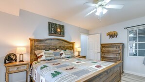 Quarto com cama de madeira, ventoinha no teto, mesa de cabeceira com abajur, cômoda e porta.