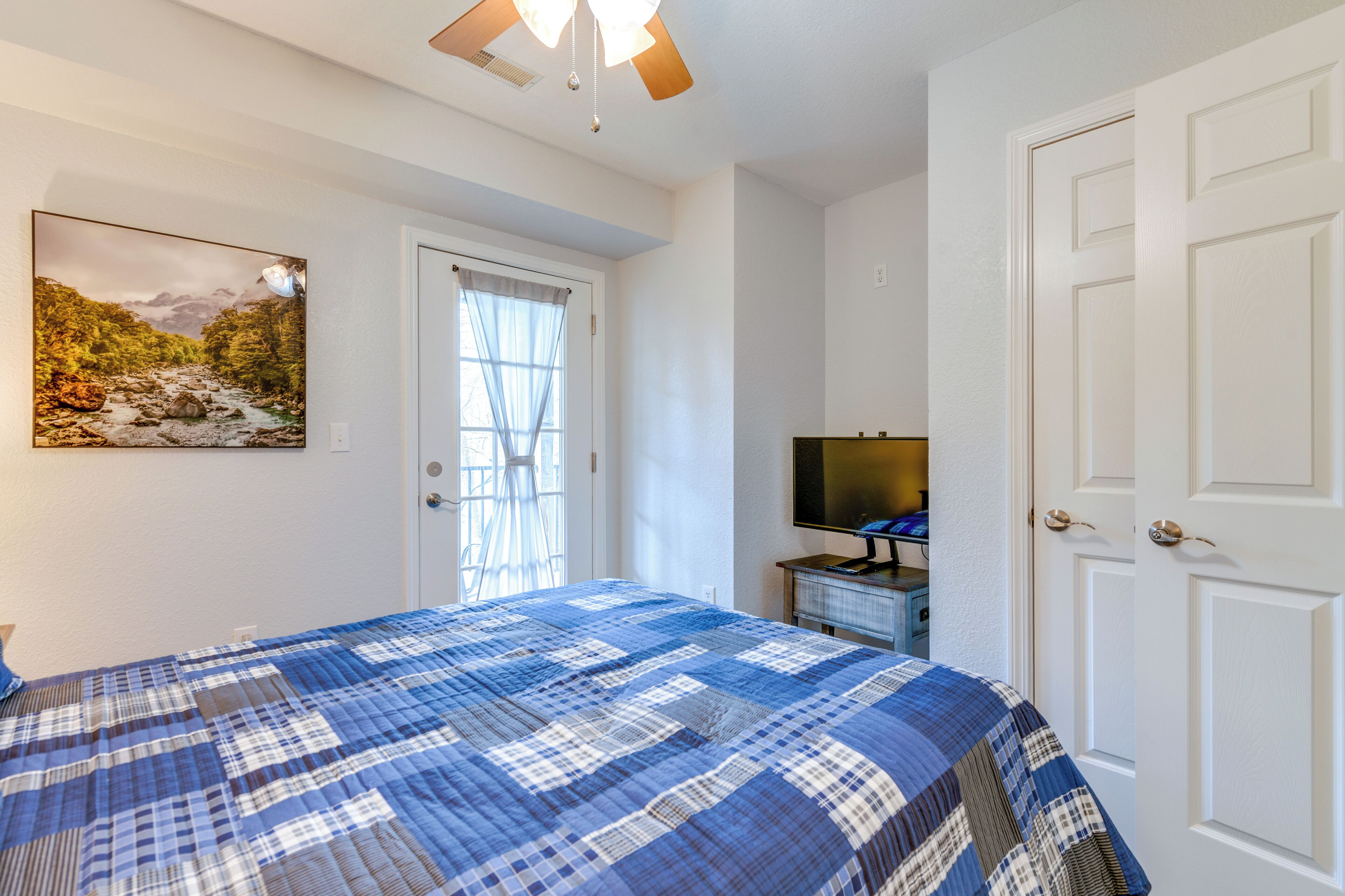A bedroom with a bed, a television on a dresser, a door, and a window with curtains.