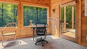 A wooden cabin interior with a desk, two chairs, large windows, and a door leading outside. - Forest Sanctuary, a Lakeside Retreat (Blue Ridge)