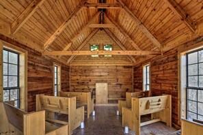 Interior de una cabaña de troncos con bancos de madera, techo alto y ventanas grandes.