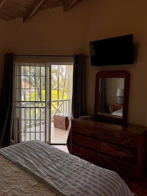 A bedroom with a bed, a dresser, a television, and a sliding glass door leading to an outdoor area with a view of palm trees. - Spacious  2 Separate Units apartment Sleeps 8 in beautiful Rodney Bay with AC (Rodney Bay)