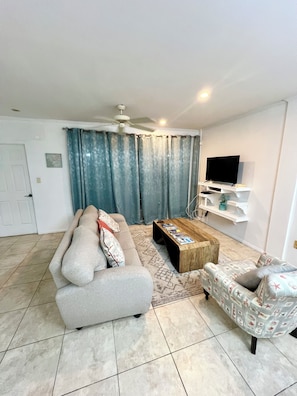A living room with a sofa, a coffee table, a television, and a ceiling fan. - Spacious  2 Separate Units apartment Sleeps 8 in beautiful Rodney Bay with AC (Rodney Bay)