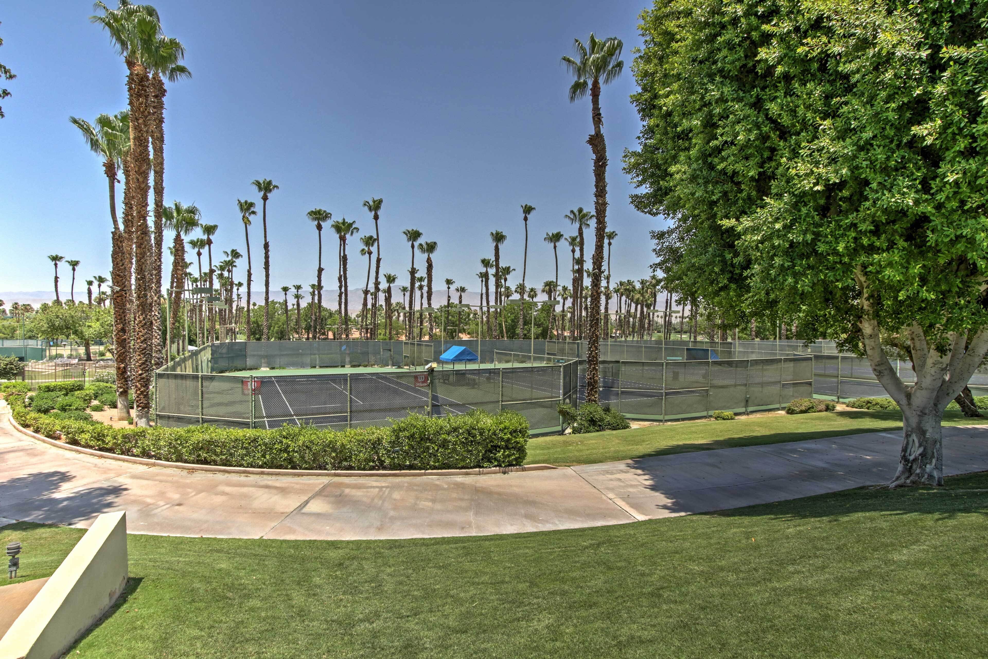Una cancha de tenis rodeada de palmeras y un césped cuidado.