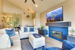 Een moderne woonkamer met een open haard, een grote televisie en een bank met blauwe kussens.