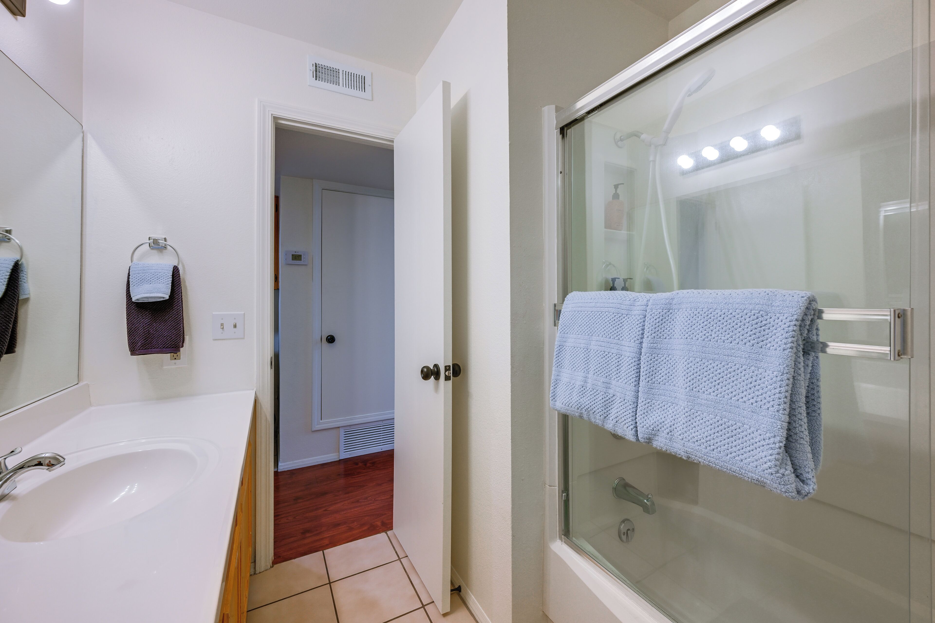 Een badkamer met een wit wastafelmeubel, een douchecabine van glas en een handdoekhouder.