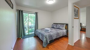 A bedroom with a bed, a window with curtains, a door, and a small table with a lamp.