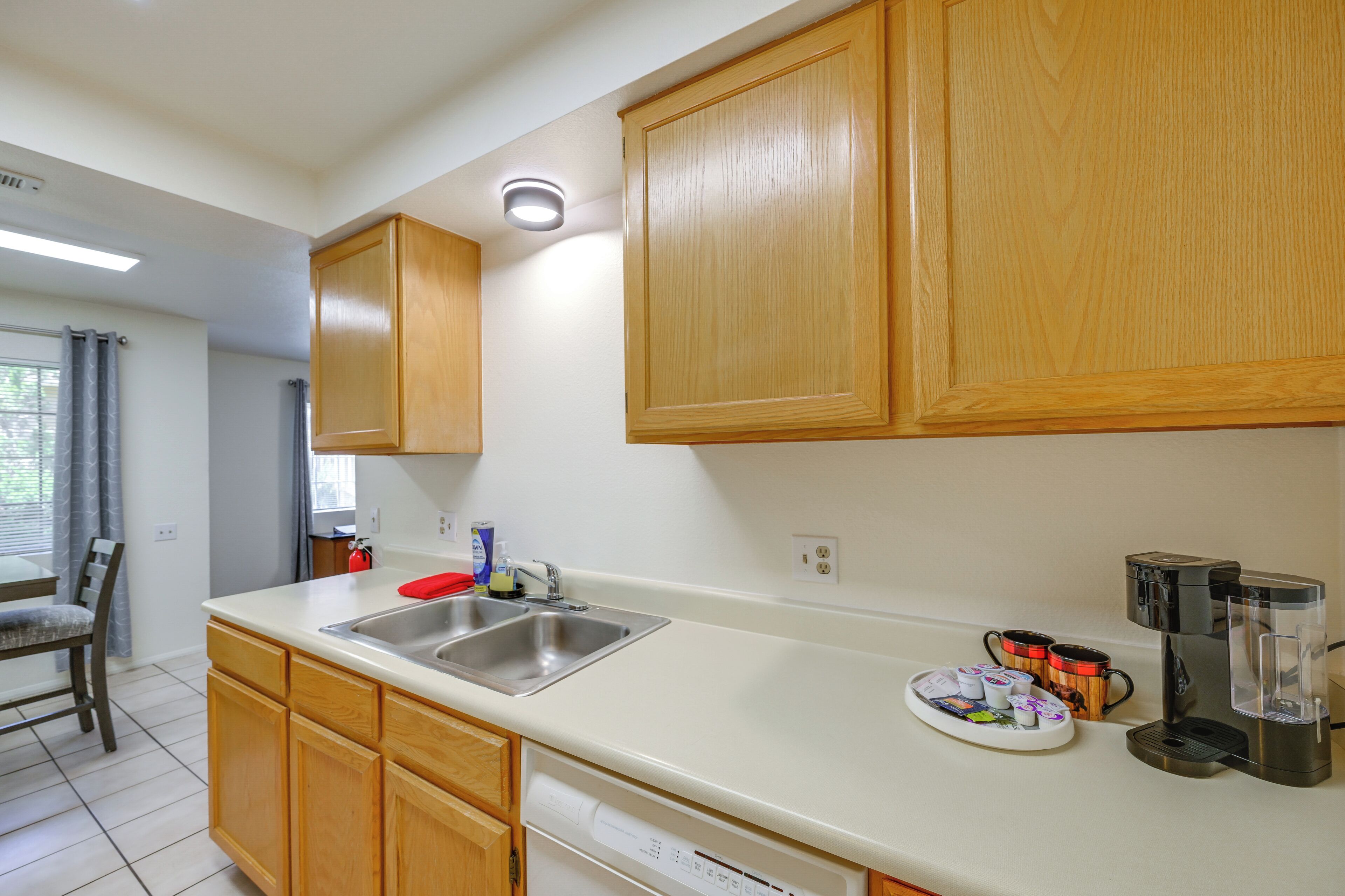 A kitchen with wooden cabinets, a stainless steel sink, a coffee maker, and a dish drying rack.