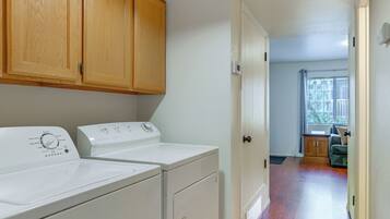 A laundry room with a washer and dryer, wooden cabinets, and a view into a living area through an open door.