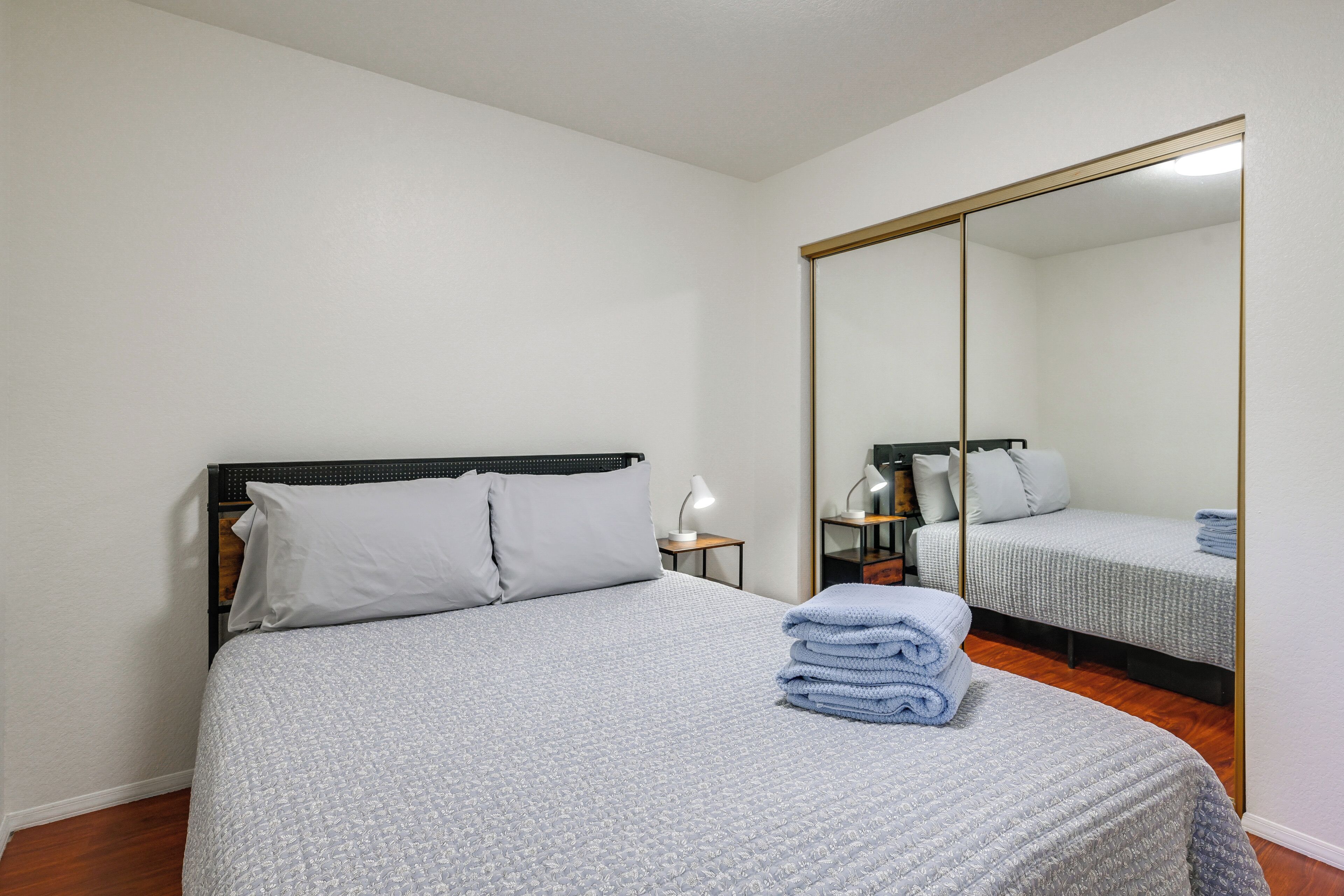 A bedroom with a bed, a nightstand, a lamp, and a large mirror.
