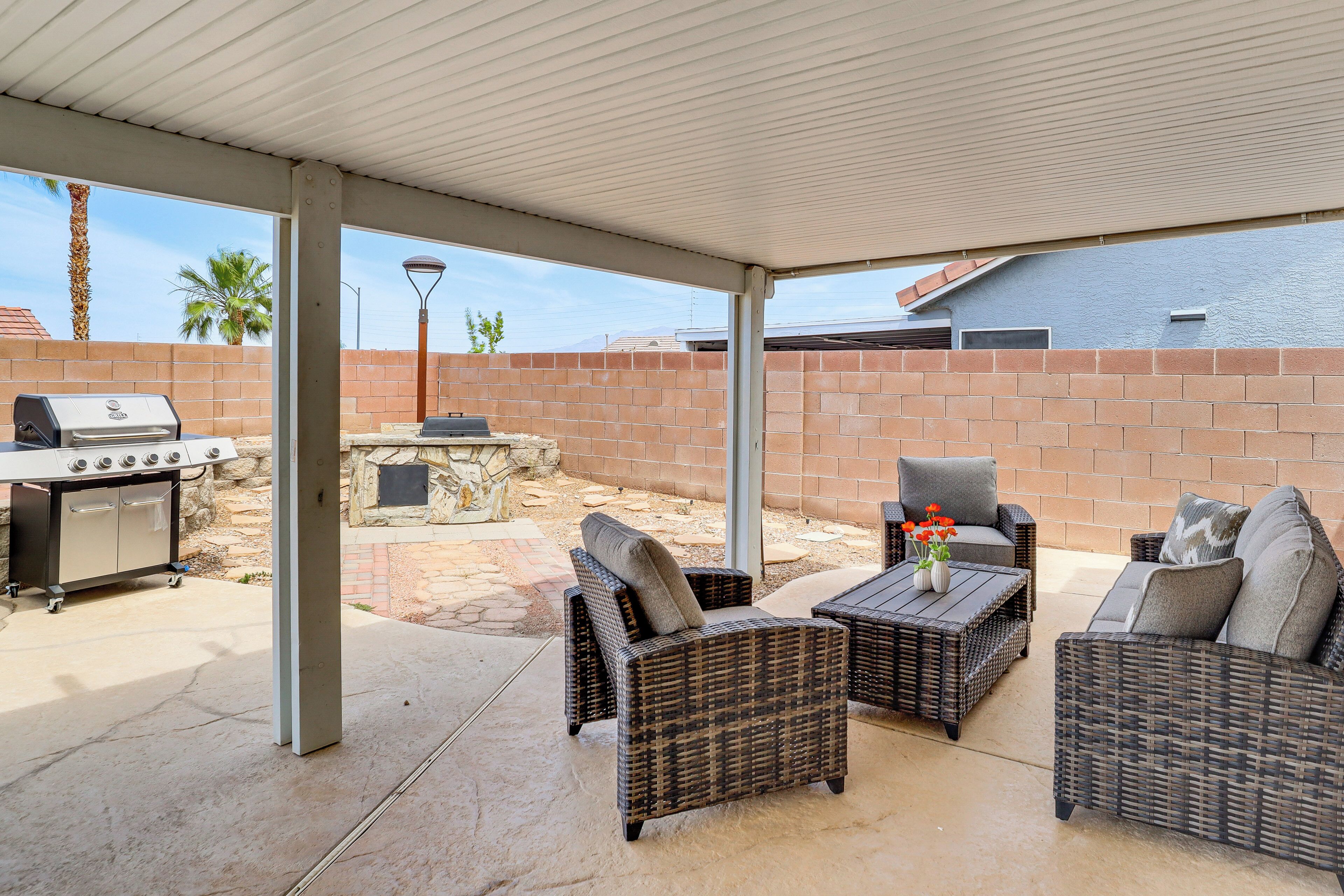 Une terrasse extérieure aménagée avec des meubles en osier, un barbecue et une cheminée en pierre.