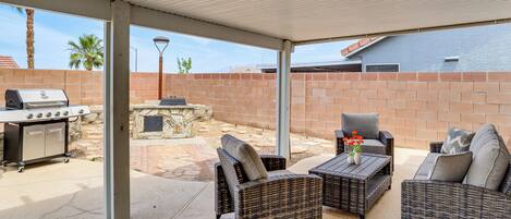 Une terrasse extérieure aménagée avec des meubles en osier, un barbecue et une cheminée en pierre.