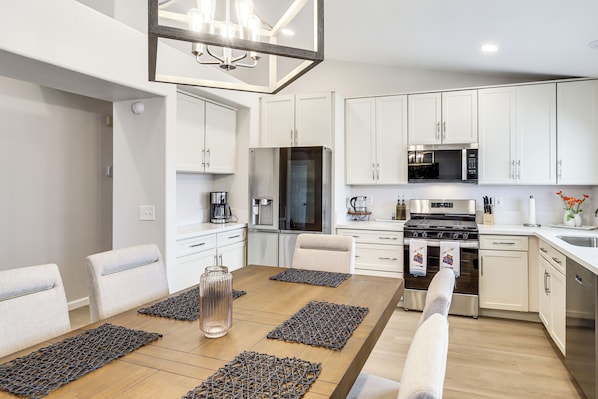 A modern kitchen with white cabinets, stainless steel appliances, and a dining area with a wooden table and chairs.