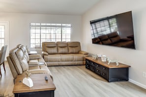 A living room with a leather sofa, a wooden coffee table, a TV mounted on the wall, and a large window. - Poolside Chills, Hiking Thrills! Las Vegas Retreat (Las Vegas)