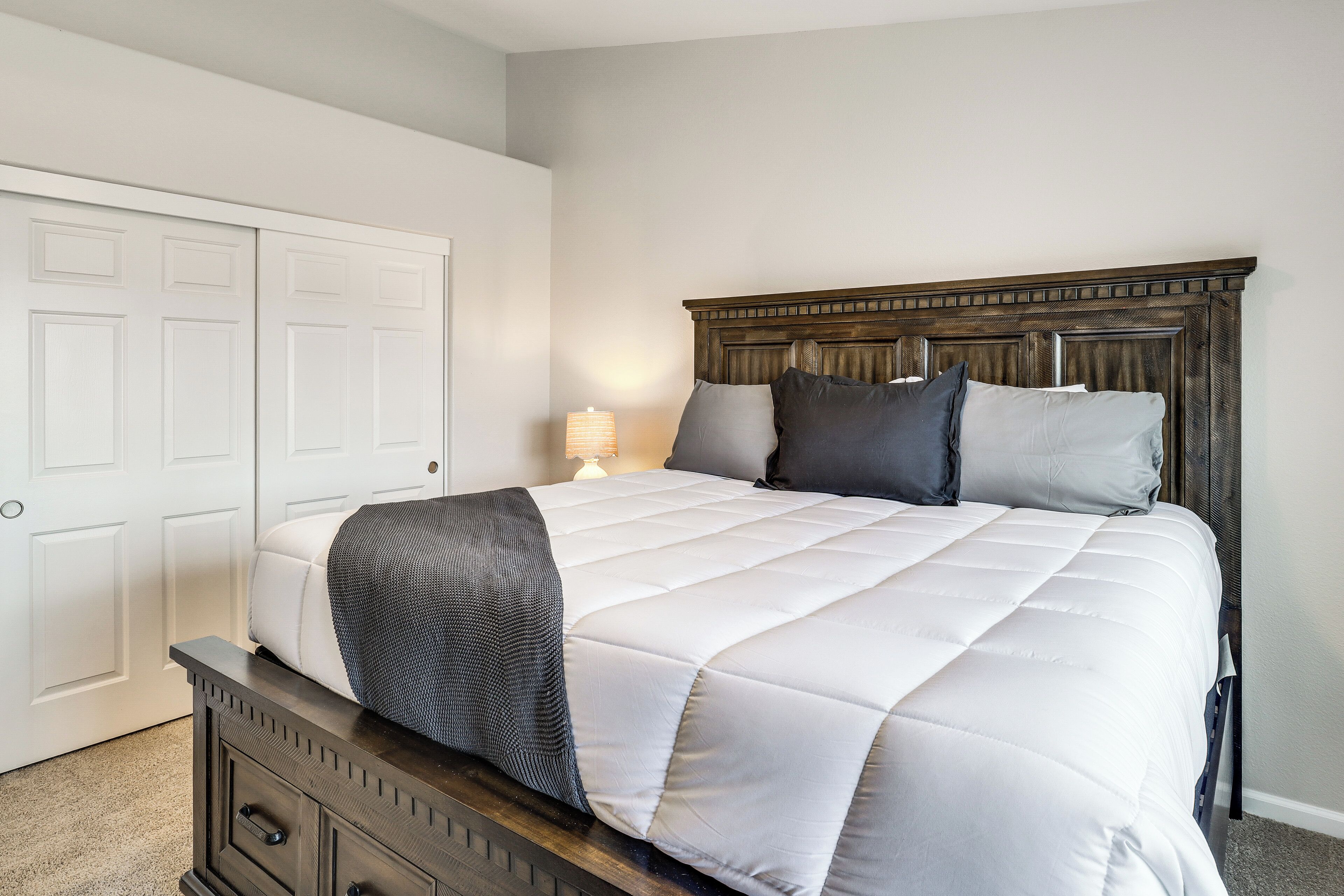A bedroom with a bed, a nightstand, a lamp, a dresser, and a closet.