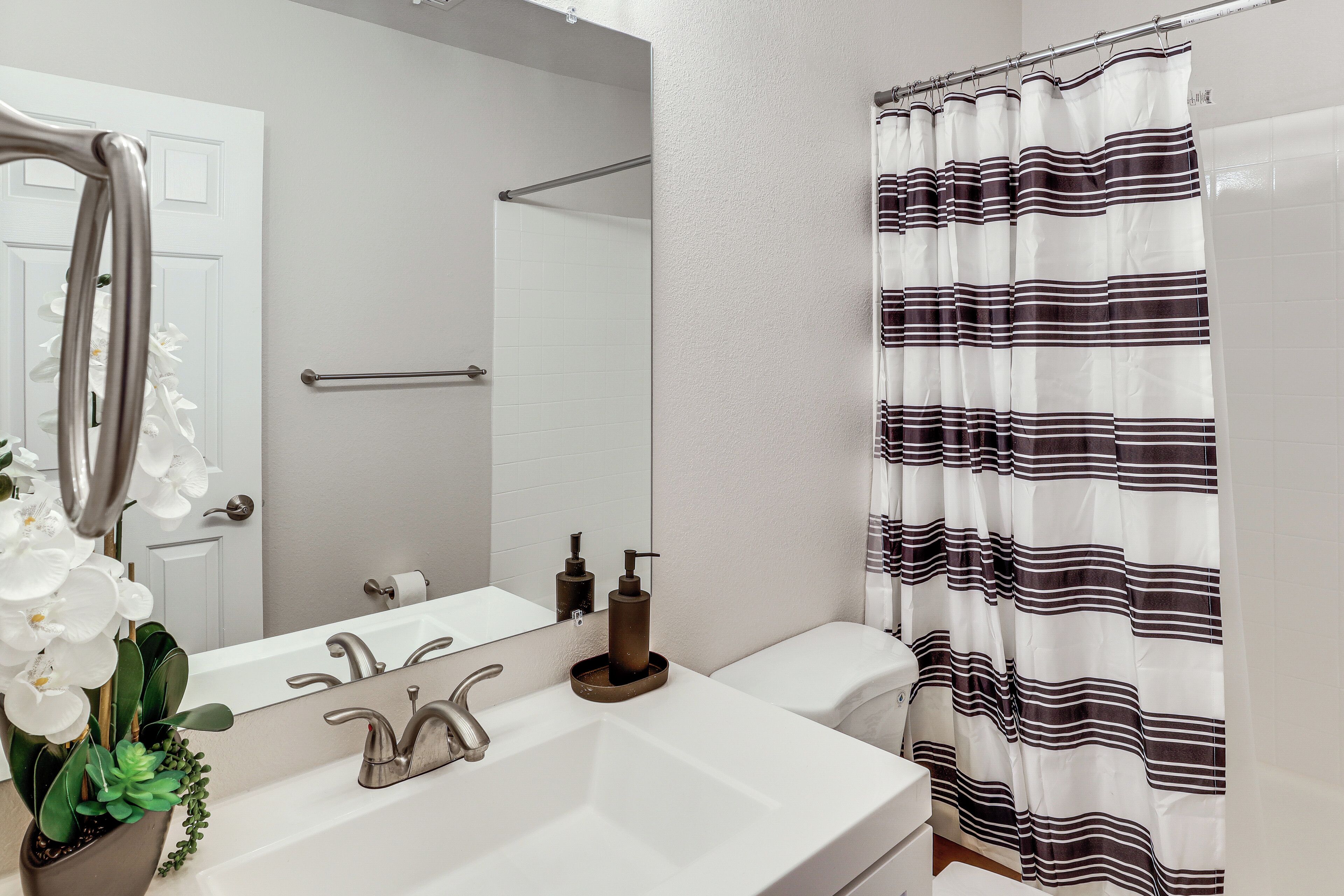 A bathroom with a white sink, a mirror, a towel rack, a shower curtain, and a toilet.