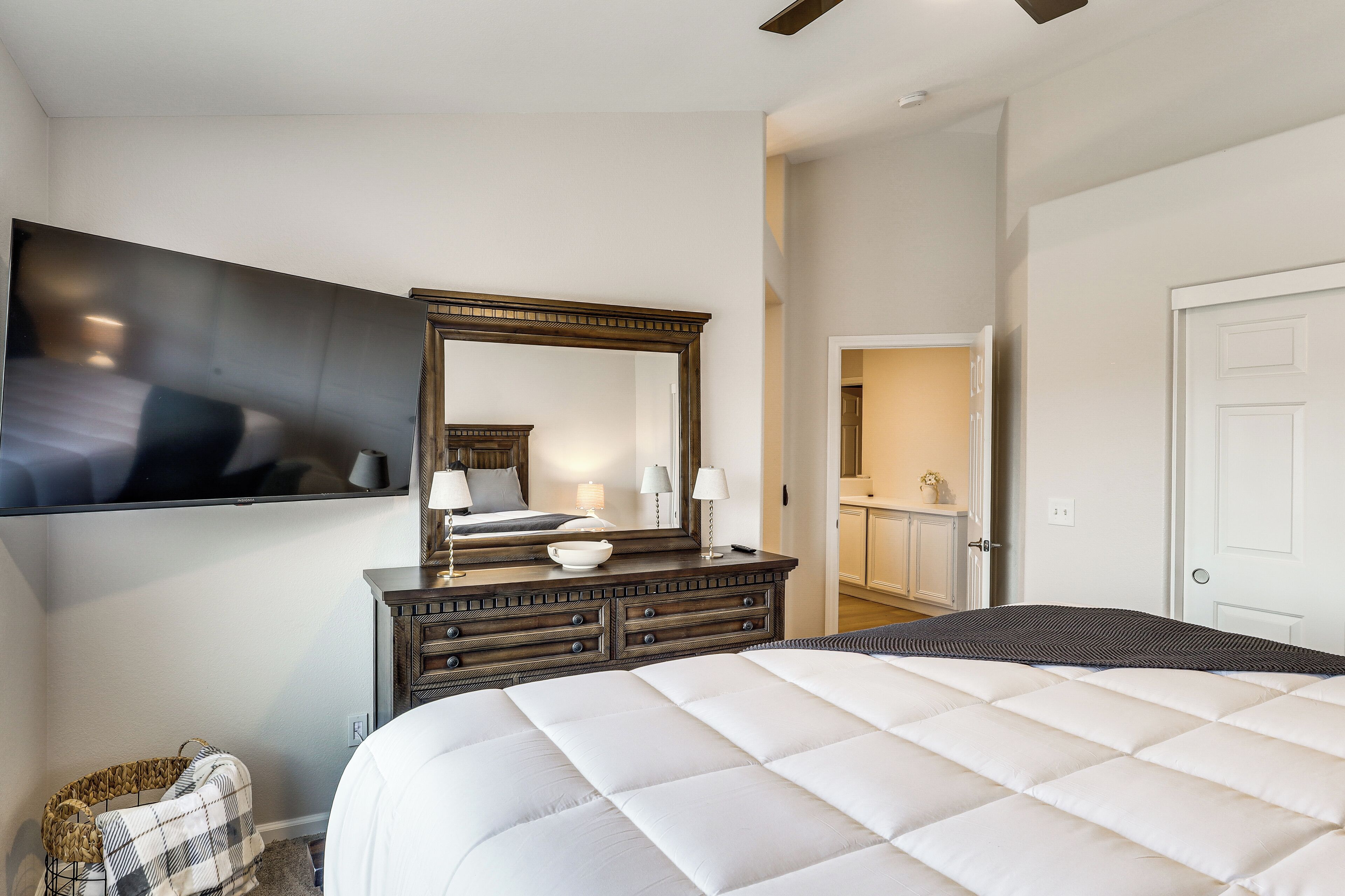 Een slaapkamer met een groot bed, een kaptafel met spiegel, een aan de muur bevestigde televisie en een deur naar een badkamer.