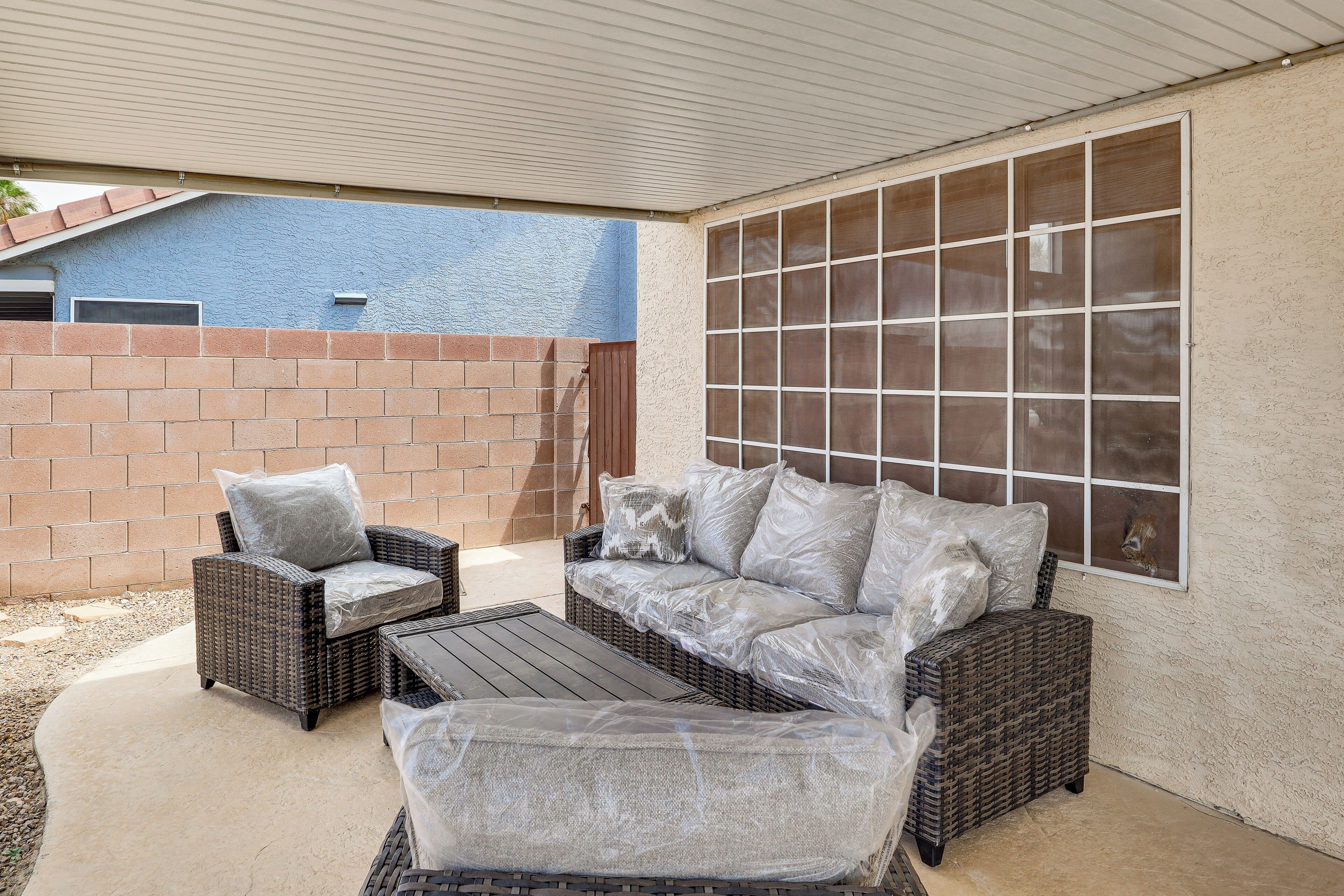 An outdoor patio area with wicker furniture, a covered ceiling, and a view of a building in the background.