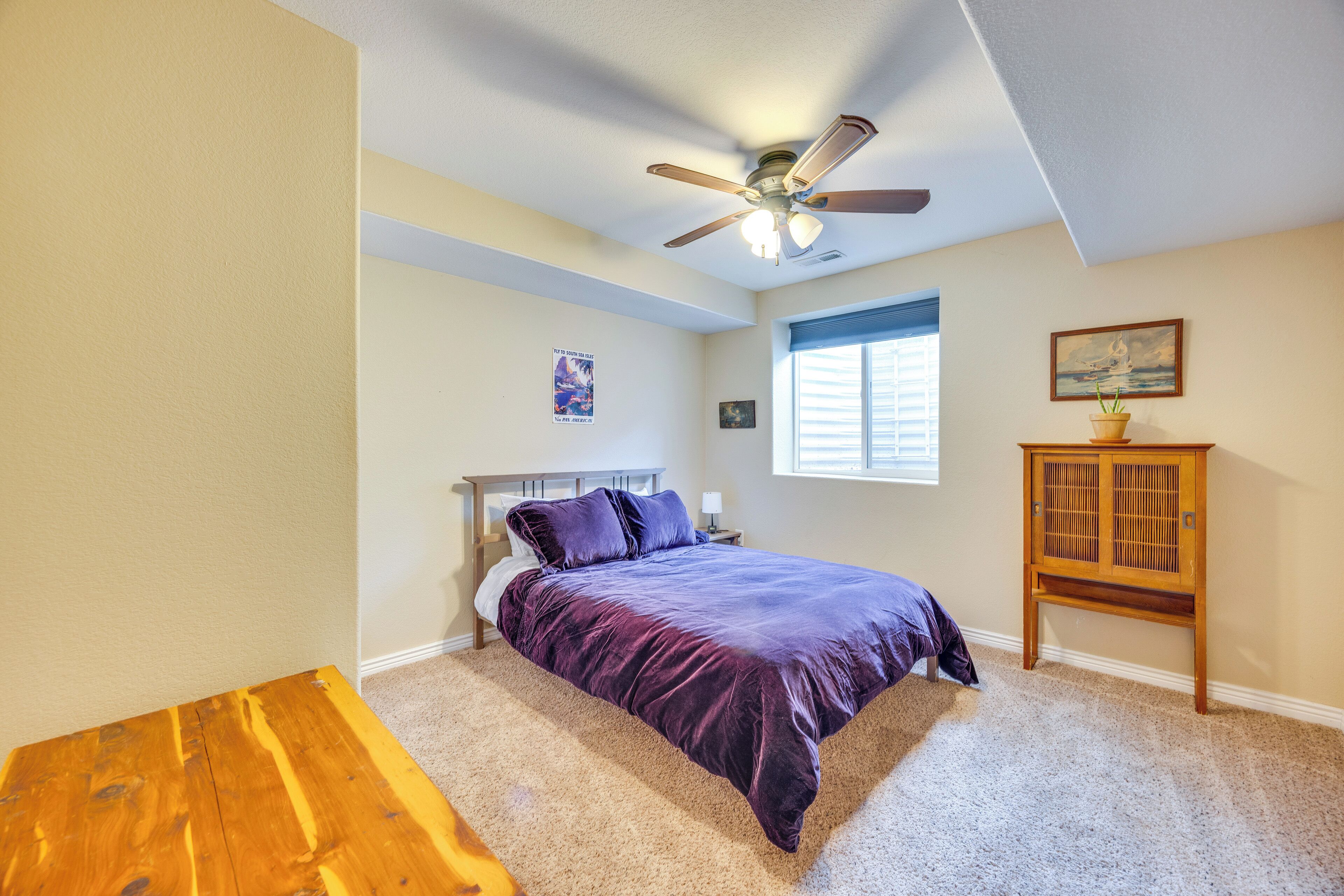 A bedroom with a bed, a ceiling fan, a window, and a wooden cabinet.
