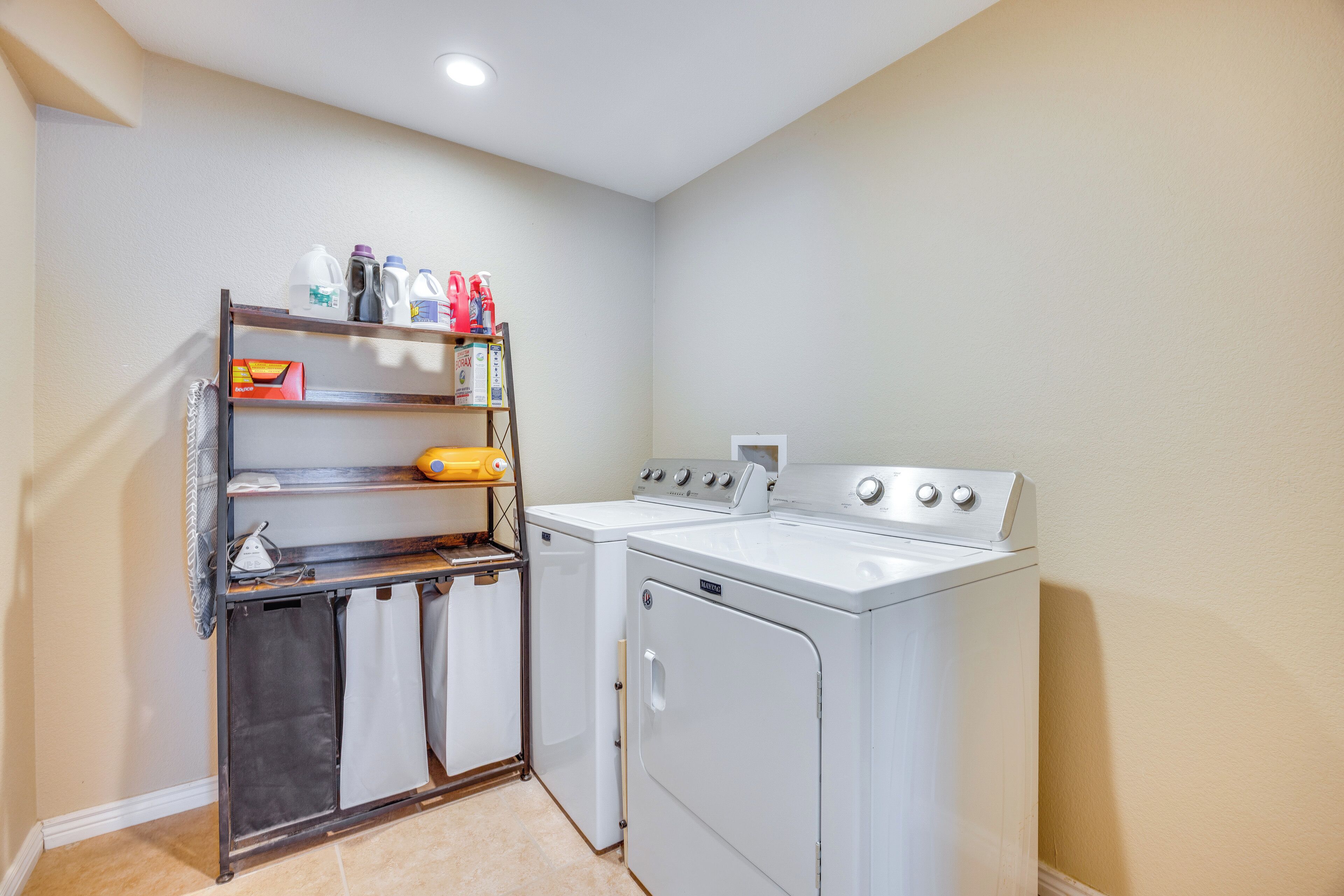 A laundry room with a washing machine, dryer, and shelves with laundry supplies.
