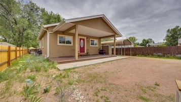 A single-story house with a covered porch, a red door, and a gravel driveway.