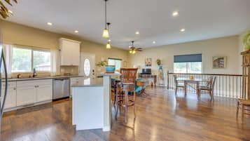 A spacious kitchen with wooden flooring, white cabinetry, and a dining area with a table and chairs.